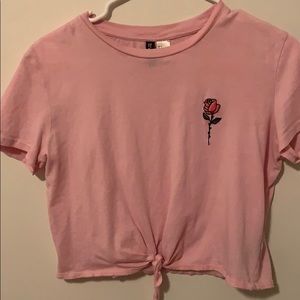 A pink crop top with a tie and flower in the front